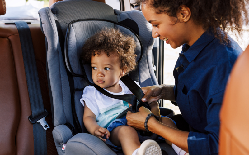 A mother secures her young child in a car seat before traveling.