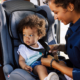 A mother secures her young child in a car seat before traveling.