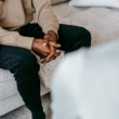 A person sits with their hands clasped while speaking with a mental health professional.
