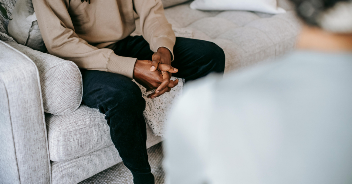 A person sits with their hands clasped while speaking with a mental health professional.