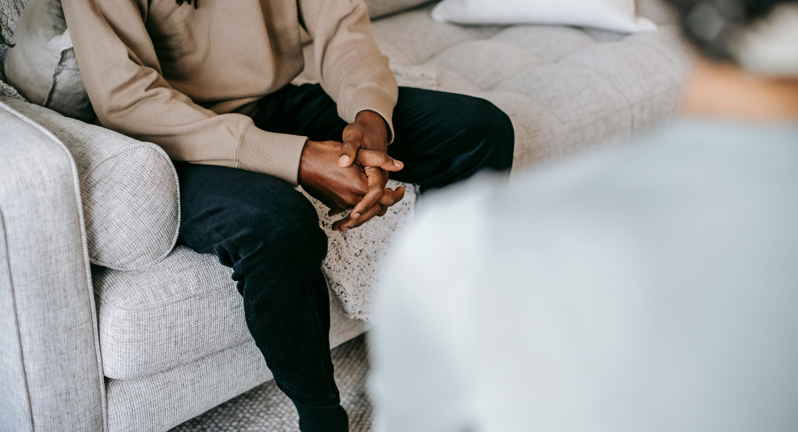 A person sits with their hands clasped while speaking with a mental health professional.