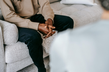 A person sits with their hands clasped while speaking with a mental health professional.