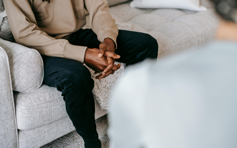 A person sits with their hands clasped while speaking with a mental health professional.