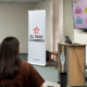 A presenter speaks to attendees during an informational session at the El Paso Chamber, standing beside a screen displaying a step-by-step process while participants listen and take notes.